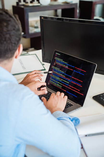Photograph of a computer screen displaying a blurry, close-up view of colorful lines of code in various programming languages, including keywords, functions, and variables, with a focus on the mix of